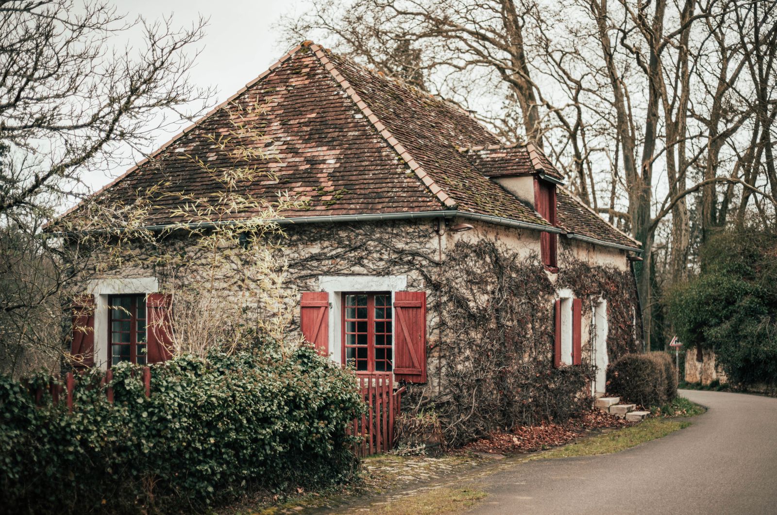 Maison de pierre à volets rouges au bord d’une route de campagne
